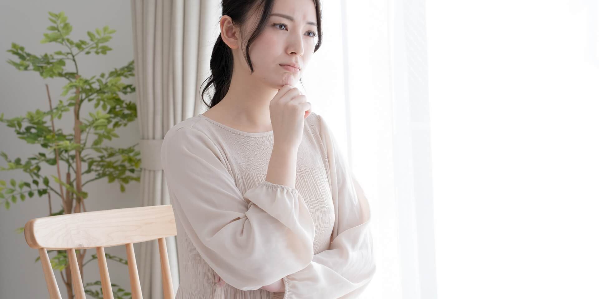 右手をあごに当てて考え込む若い女性