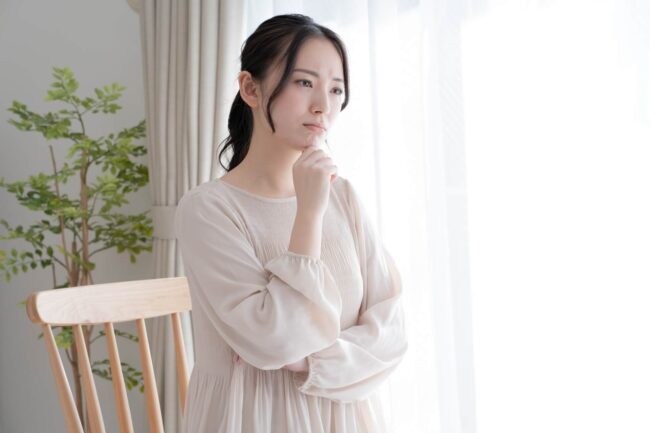 右手をあごに当てて考え込む若い女性